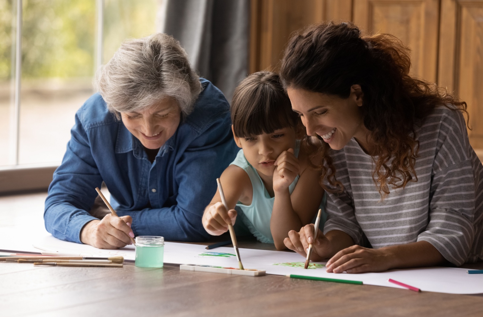 A young girl paints with her mother and grandmother