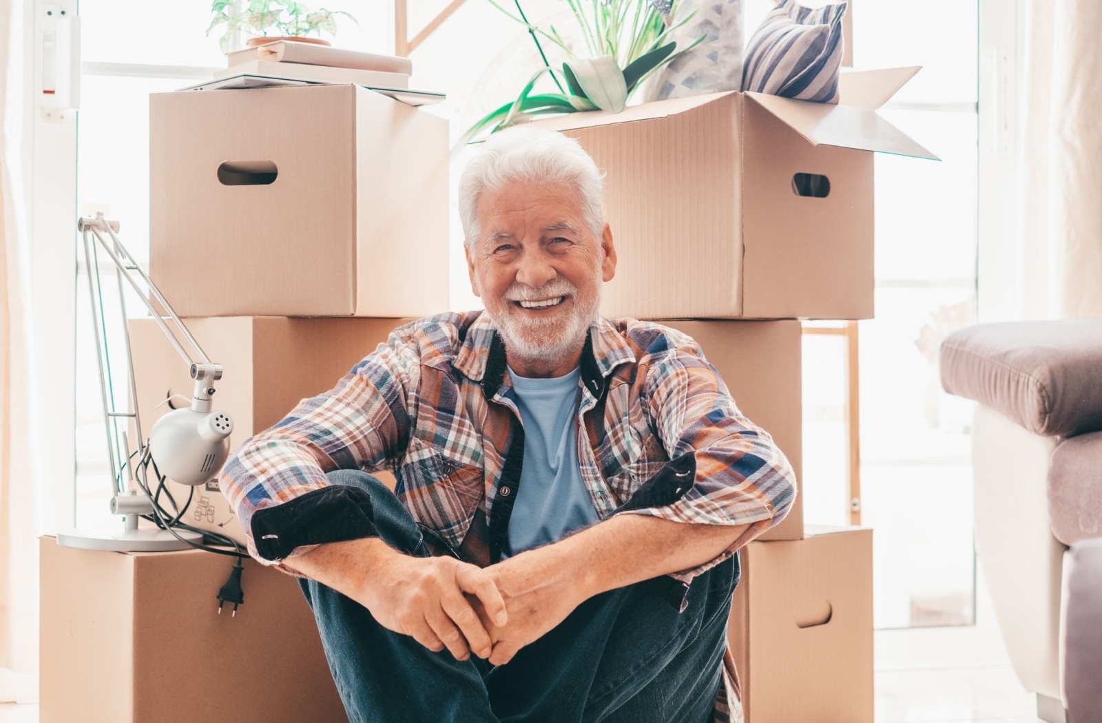 A senior man sitting and smiling in front of moving boxes as he transitions to assisted living.