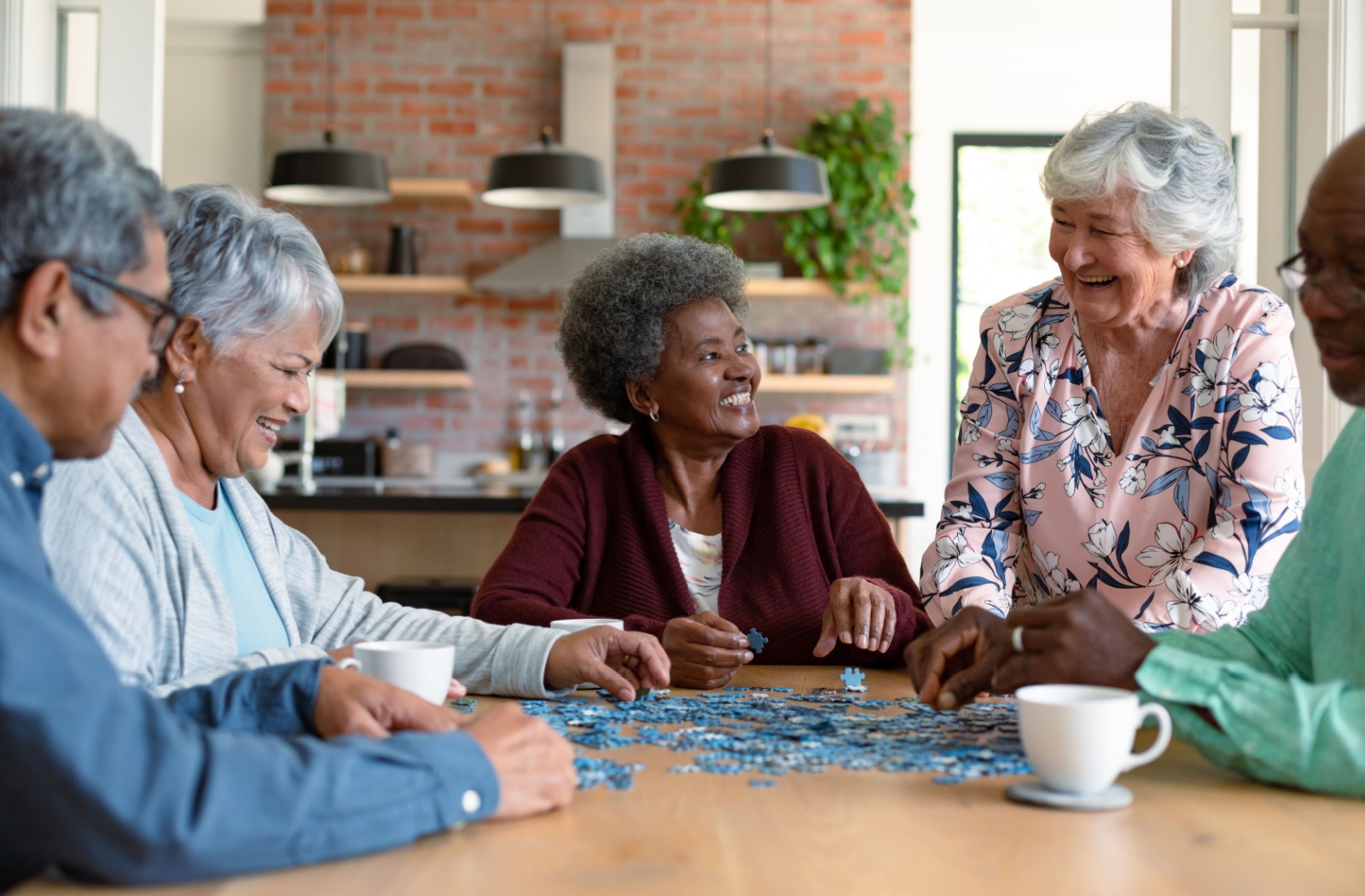 A group of seniors sitting around a table laughing while doing a puzzle in senior living.