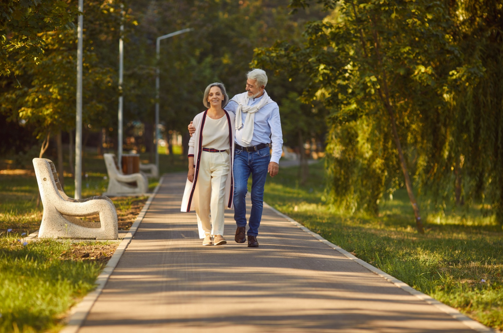 An older adult couple walking outdoors on a path in a park.