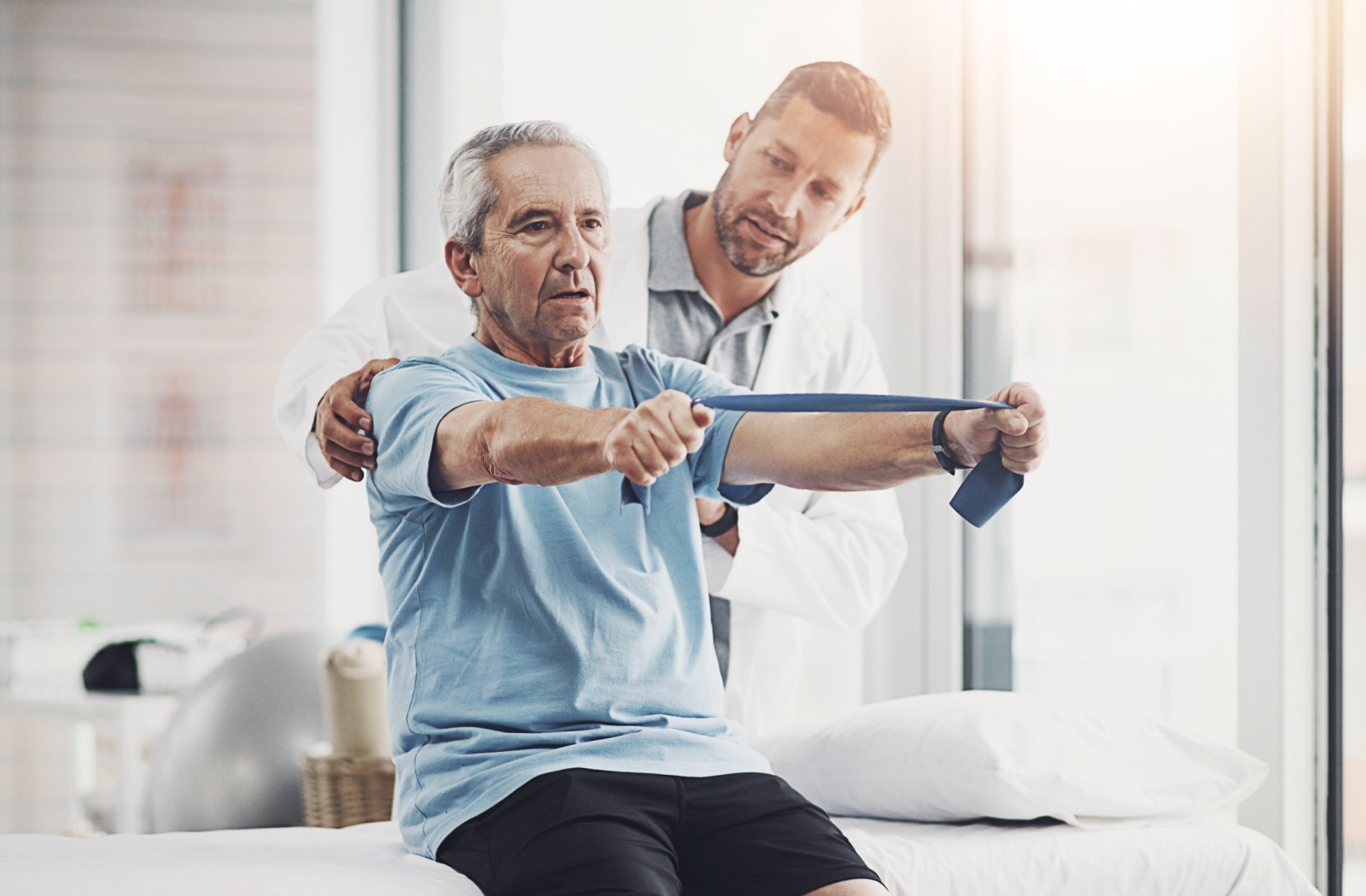 A physical therapist helps a senior exercising with a resistance band.