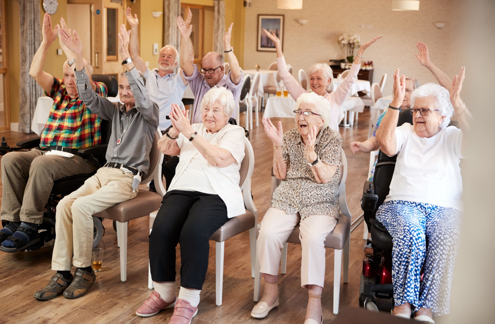 A group of seniors sitting in chairs at a community center clapping and cheering.