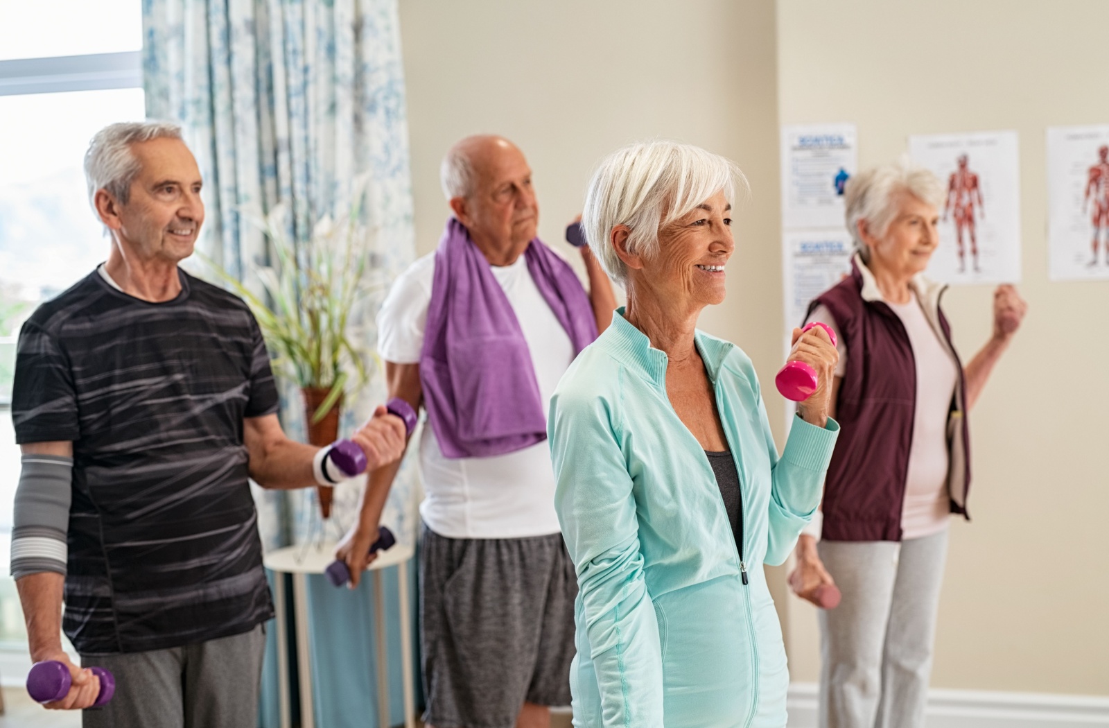 A group of four seniors standing and doing bicep curls with dumbbells while smiling
