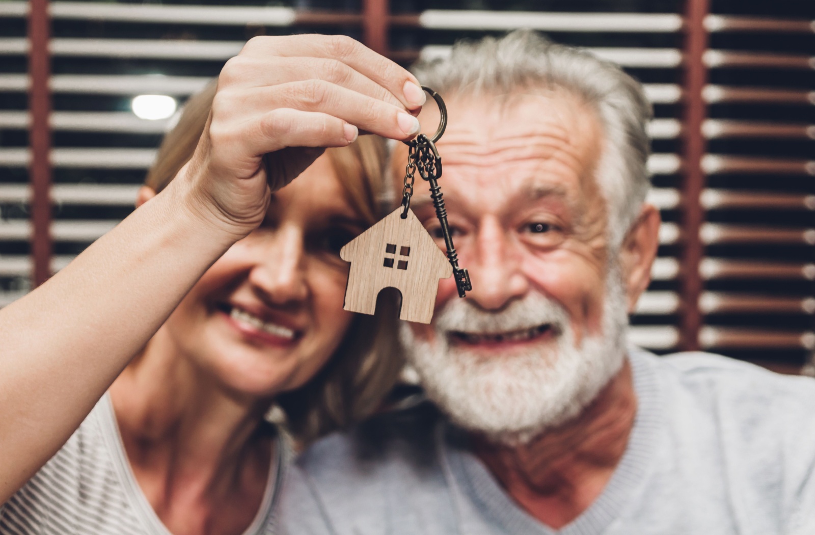 An older couple smiles while holding up a keychain with a key and a small house on it