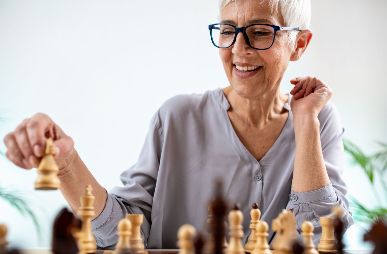 An older adult laughs while moving a knight during a chess game against a fellow resident in senior living