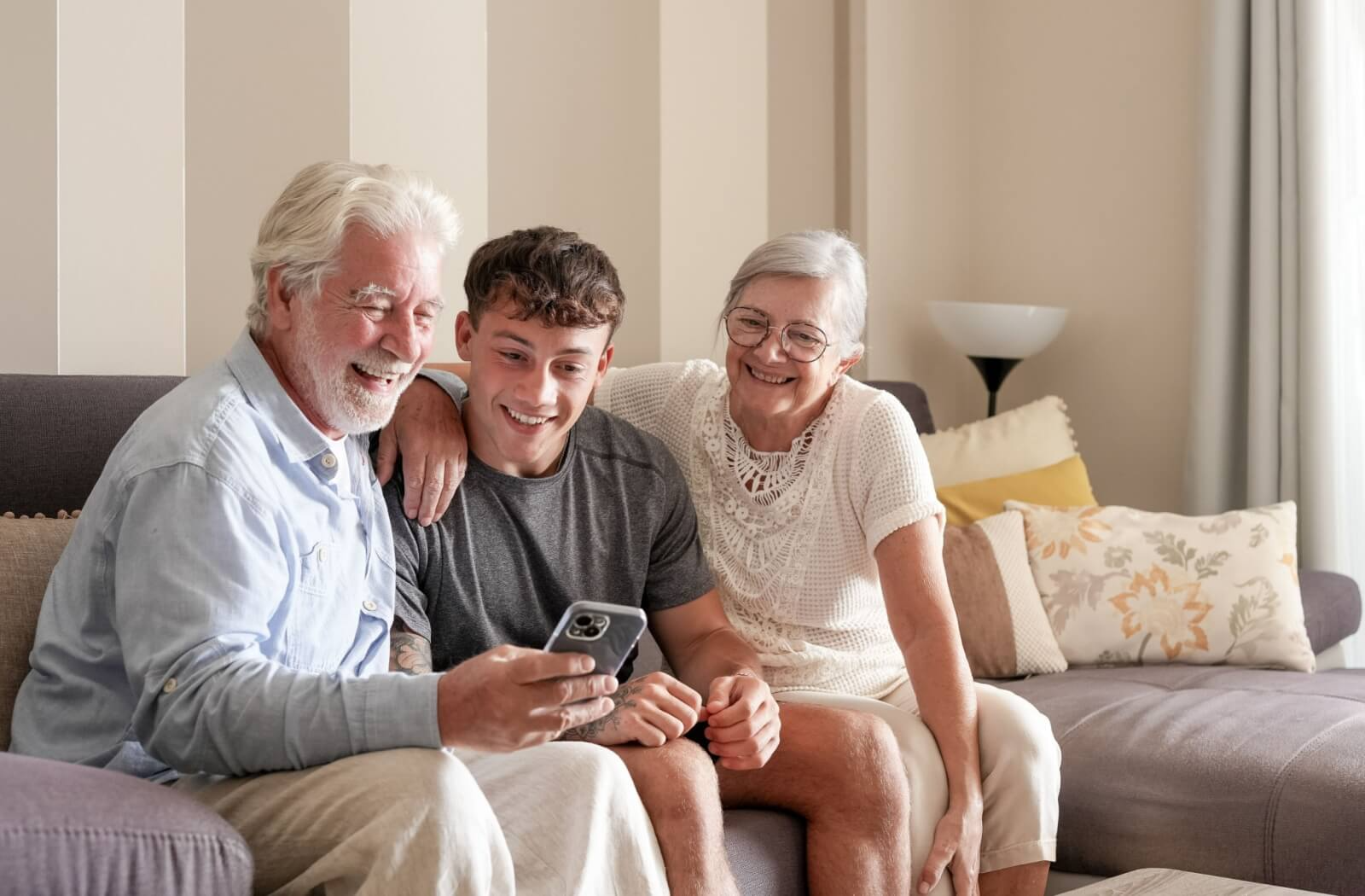 Senior couple and younger relative smile during a family conversation while looking at a phone
