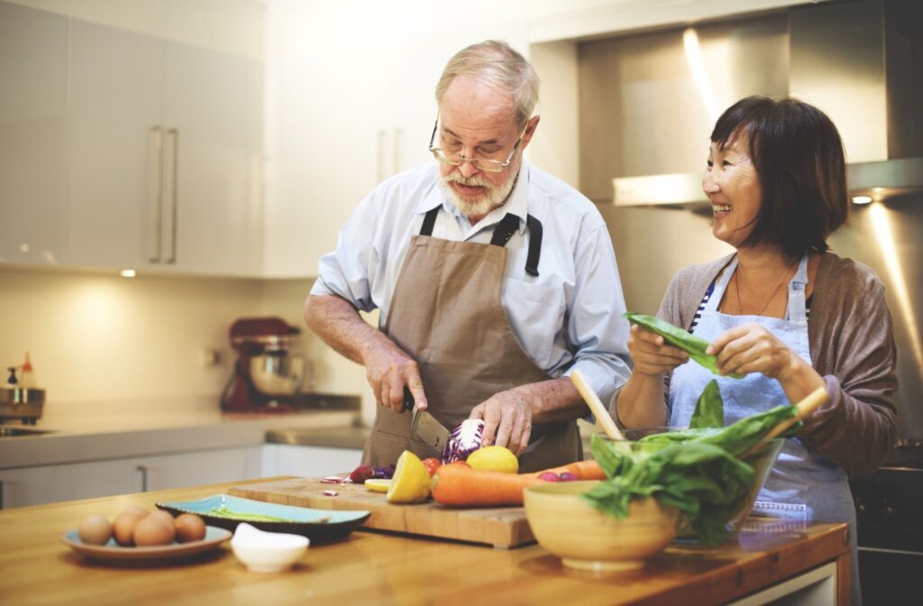 A senior couple chop vegetables while preparing meals in their kitchen